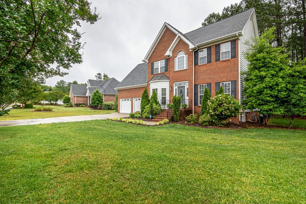 A two-story brick house with black shutters, an arched window, a two-car garage, and a manicured front lawn.